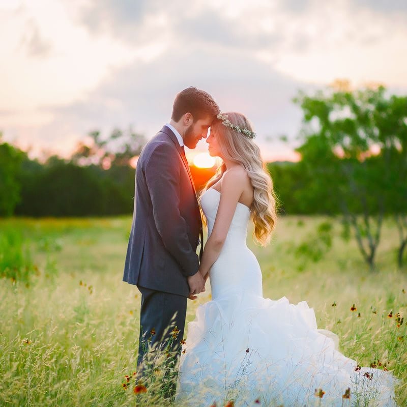 Bride and groom tap foreheads together at sunset in a field