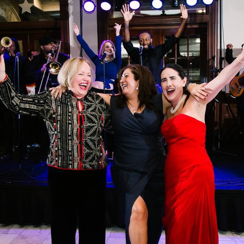 Three middle aged women happily dance at reception together