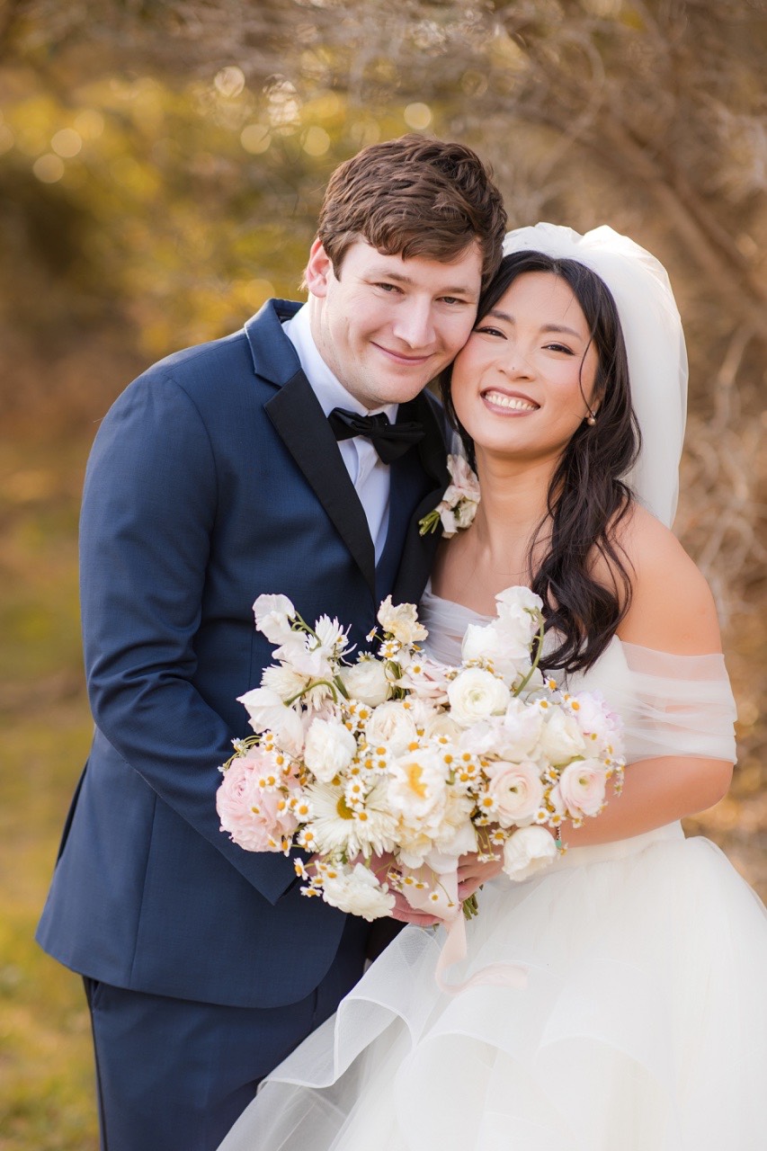 L and M embracing near trees at Pecan Springs Ranch wedding location